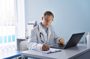 Healthcare professional reviewing patient information and taking notes in a clinical office setting.