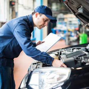 Mechanical Engineering inspecting a car engine in a workshop with a clipboard.