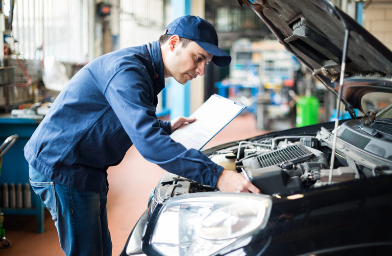 Mechanical Engineering inspecting a car engine in a workshop with a clipboard.