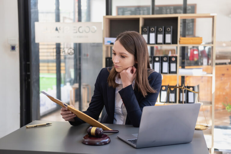 A professional woman working as a legal secretary, sitting at a desk with legal documents, a gavel, and a laptop in an organized office environment.